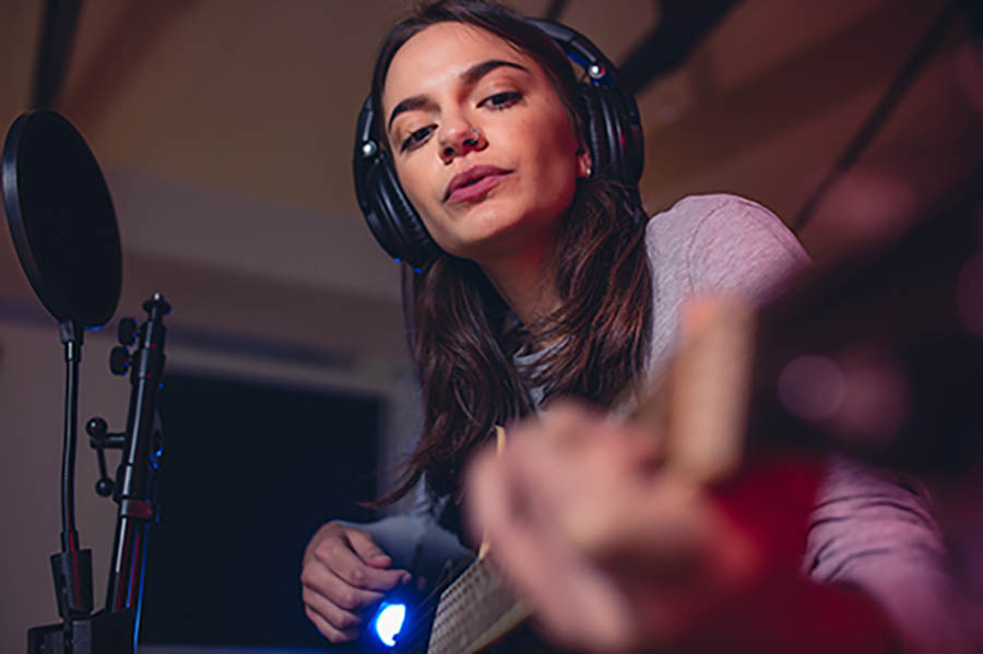 Woman guitarist playing guitar in a recording studio. Female singer singing a song in studio.