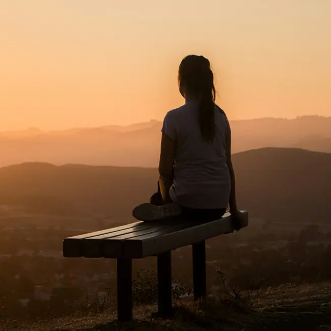 Person sitting on a bench overlooking mountains at sunset
