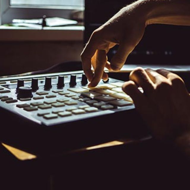 Close-up of hands using a keyboard and turning knobs on an audio mixing console in a dim studio.