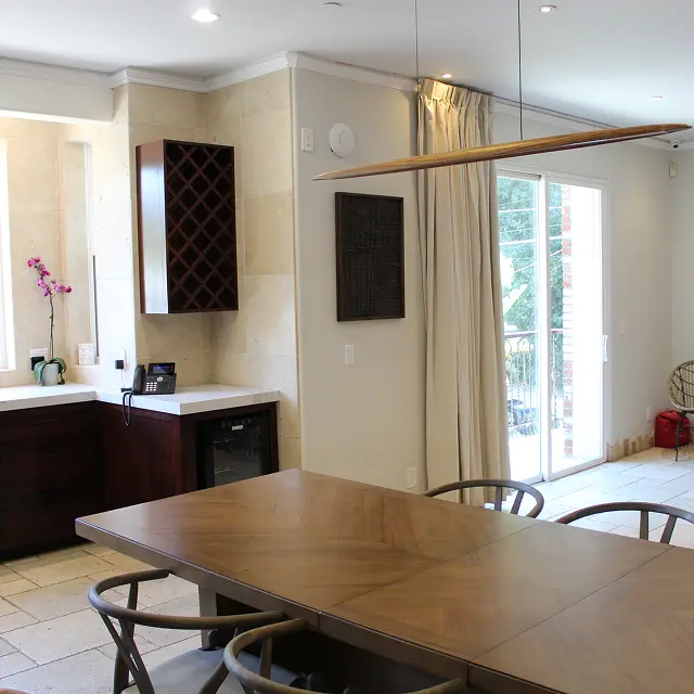 Bright living area with a wooden dining table, tall curtains, large windows to a patio, and built-in wall niches with speakers or panels.
