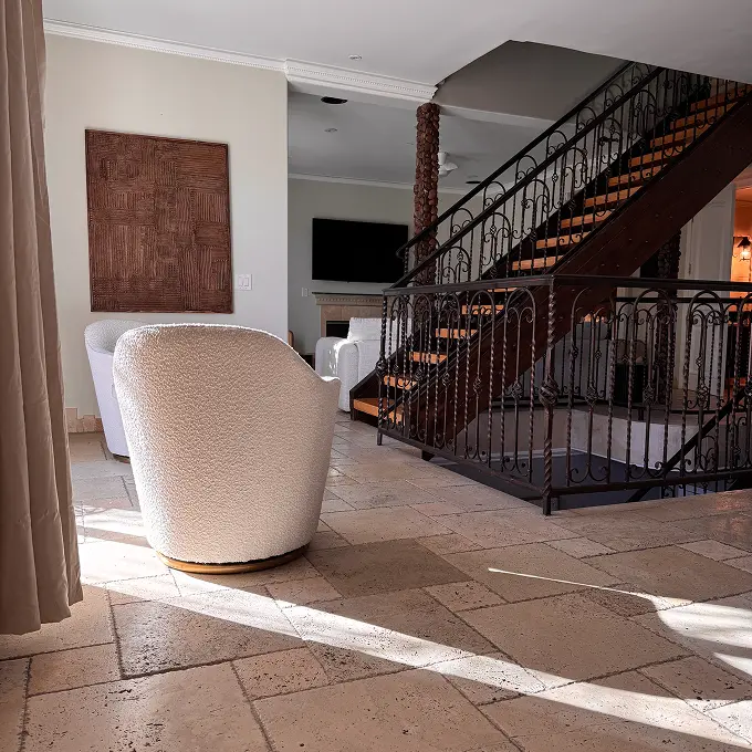 Living room interior with a curved staircase and wrought-iron railing, featuring a white upholstered chair in the foreground on tiled floors.
