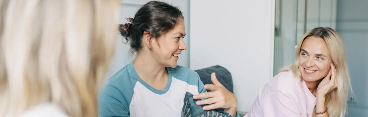 A healthcare worker in blue and a woman in pink talk while smiling in a bright indoor room.