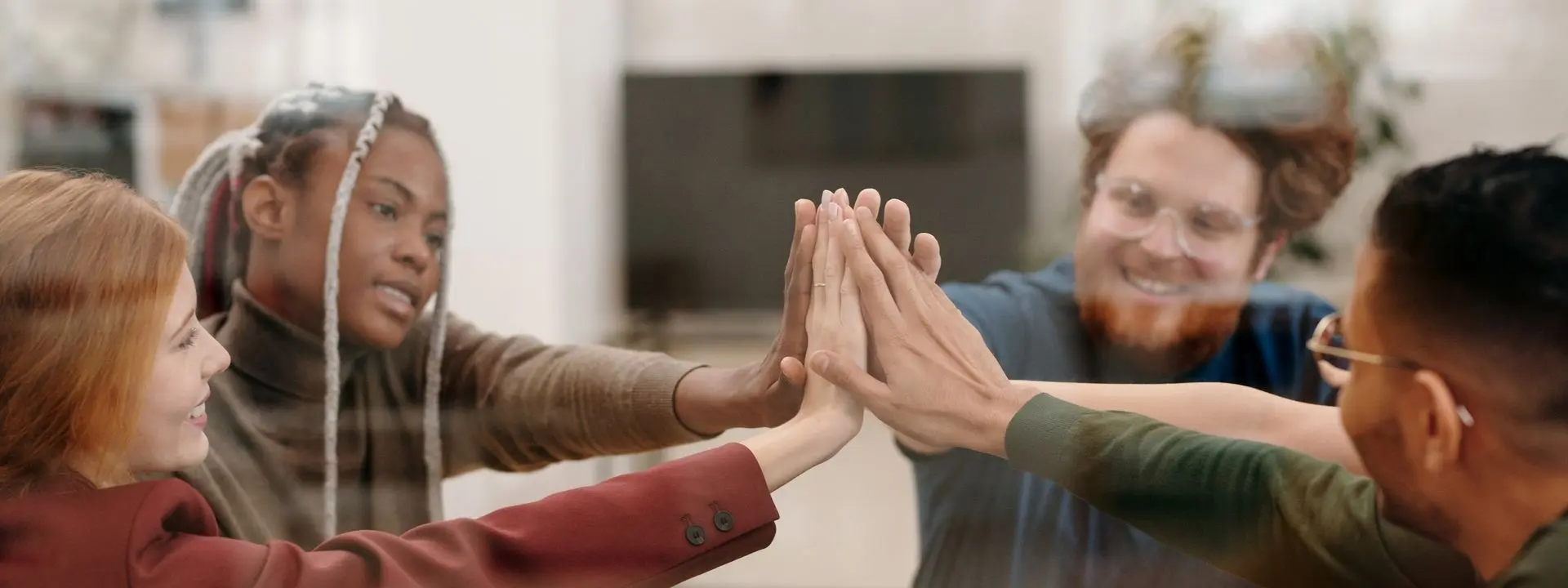 A group of people indoors hold their hands up together in a high-five/prayer-like gesture.